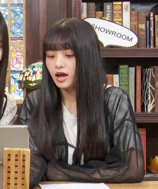 a woman with long black hair is sitting at a table in front of a bookshelf with a sign that says showroom .