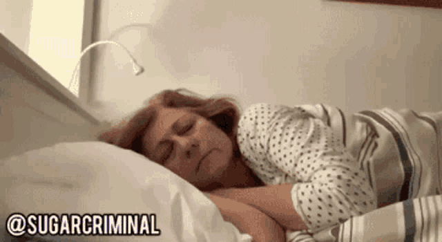 a woman is sleeping in a bed with a striped blanket and a light on the wall .