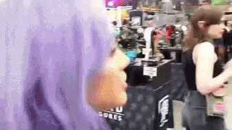 a woman with purple hair is standing in front of a table that says ' cube ' on it .