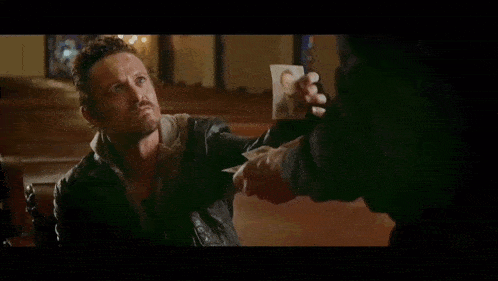 a man in a black leather jacket is talking to another man in a room .