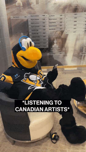 a penguin mascot wearing headphones sits in a chair