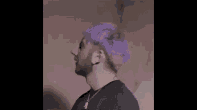 a man with purple hair and a beard is wearing a purple headband .