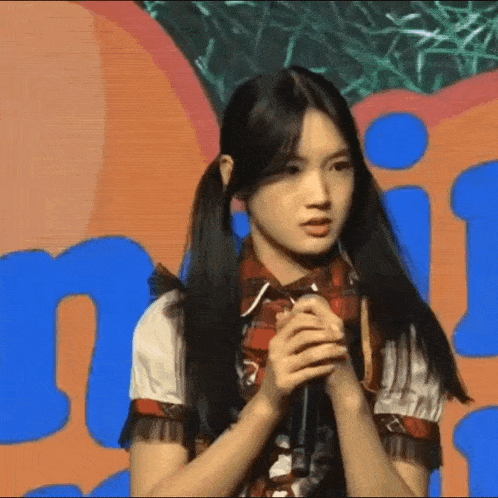 a girl with pigtails is holding a microphone in front of a sign that says n.