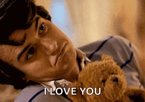 a man laying on a bed holding a teddy bear with the words i love you above him