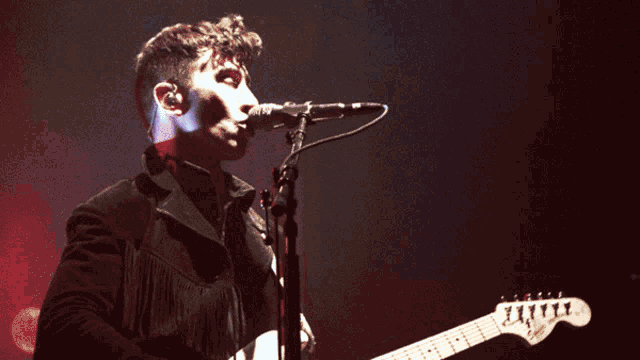 a man singing into a microphone with a guitar in front of him