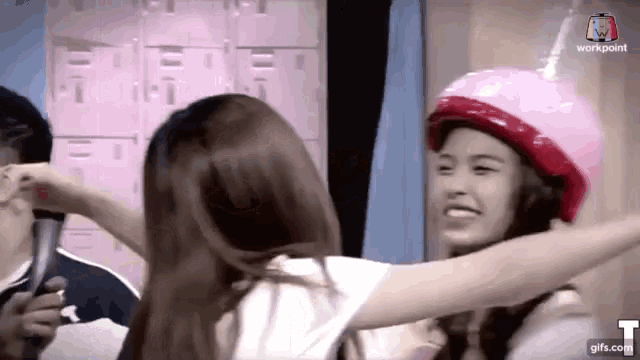 a woman wearing a pink helmet is hugging another woman wearing a white shirt .