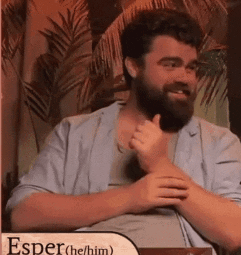 a man with a beard is giving a thumbs up while sitting in a chair .
