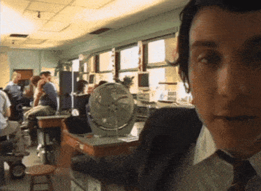 a man in a suit and tie is standing in a room with a fan