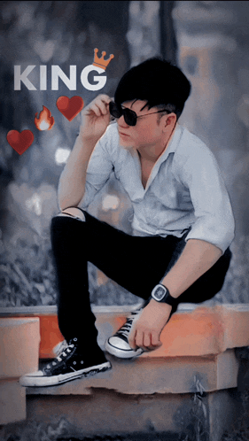 a man wearing sunglasses and a watch sits on a brick wall with the word king above him
