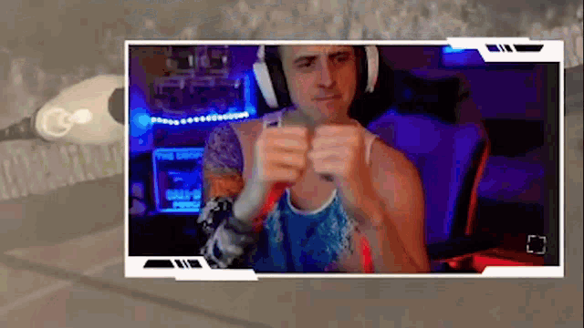 a man wearing headphones and a blue tank top is playing a video game on a computer .