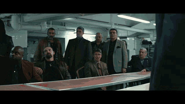 a group of men are sitting at a table in a dark room