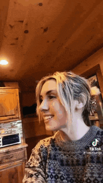 a woman wearing a sweater is smiling in a kitchen .