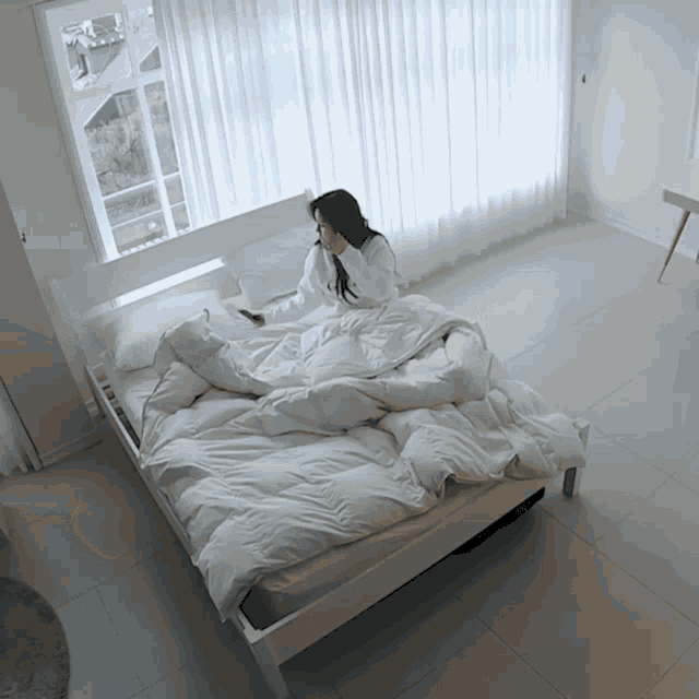 a woman is laying on a bed with a white blanket