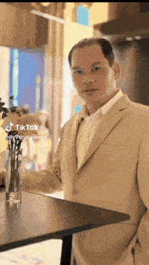 a man in a suit is standing next to a table with flowers in a vase .