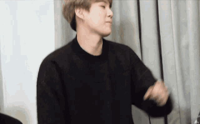a man in a black sweater is standing in front of a white curtain .