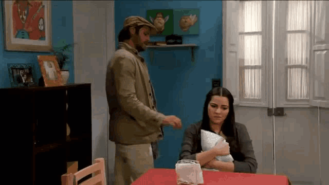 a man standing next to a woman sitting at a table with a napkin that says ' a ' on it