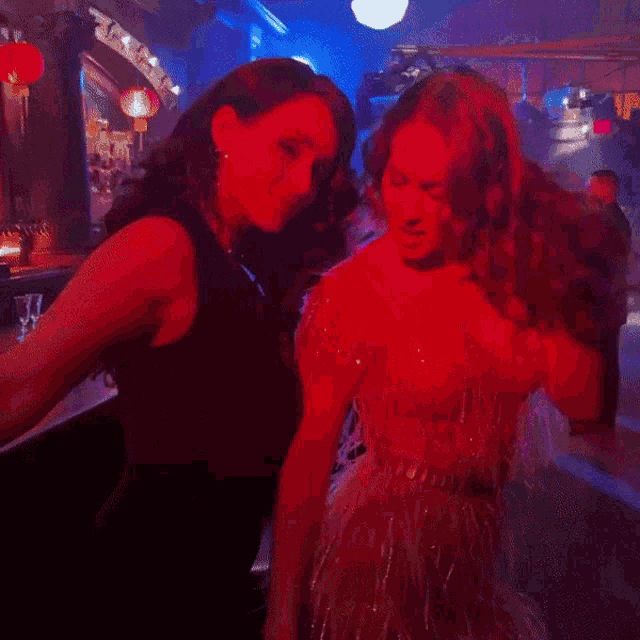 two women are dancing together in a dark room with red lights