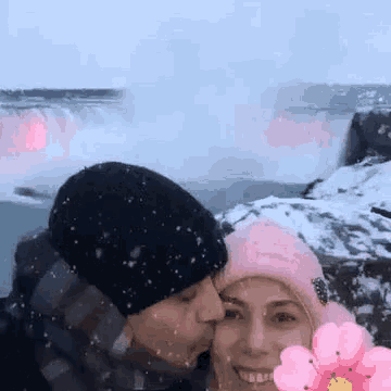 a man is kissing a woman in front of a waterfall .