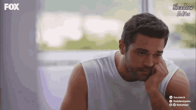 a man in a white tank top sits in front of a window with the fox logo on the bottom right