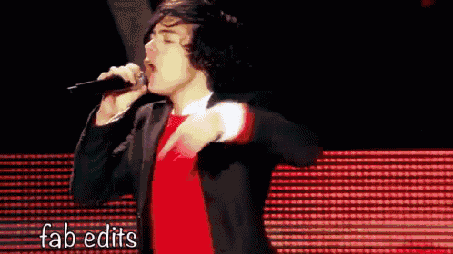 a man is singing into a microphone while wearing a red shirt and a black jacket .