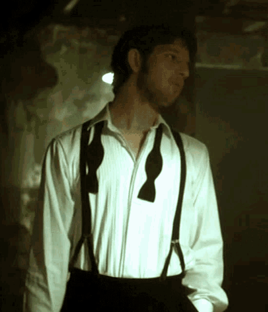 a man wearing suspenders and a bow tie looks to his left