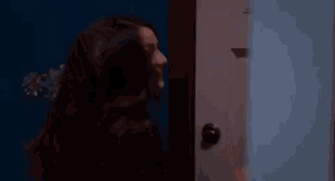 a woman with long dark hair is smiling and looking at the camera in a dark room .