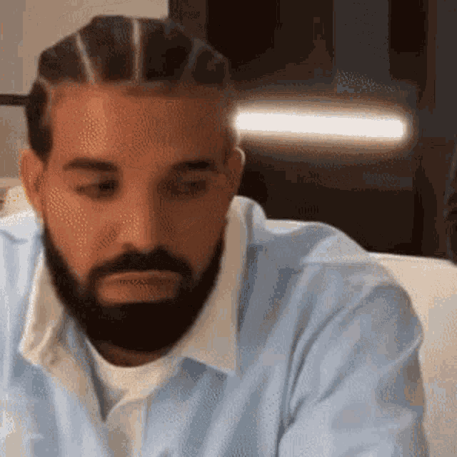 a man with a beard and braids is sitting on a couch looking down .