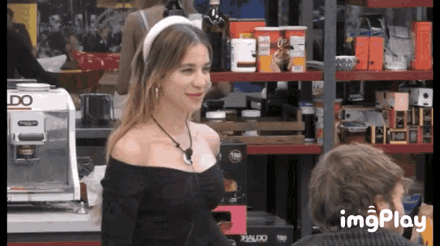 a woman in a black off the shoulder top is standing in front of a delonghi coffee maker