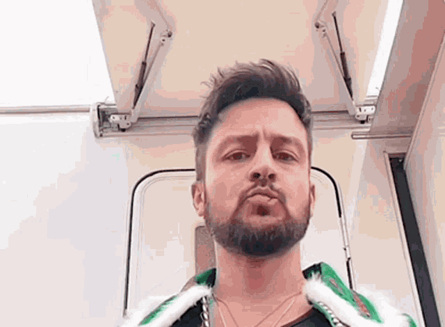a man with a beard and a green jacket is standing in front of a trailer .