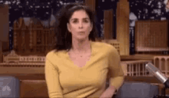 a woman in a yellow shirt is sitting in front of a microphone and making a face .