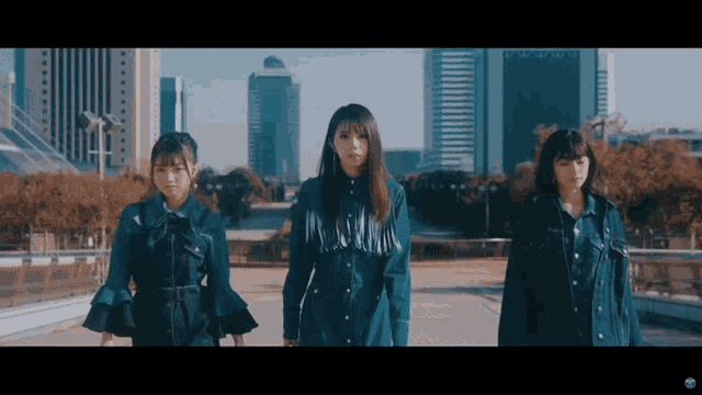 three girls in blue dresses are standing in front of a city