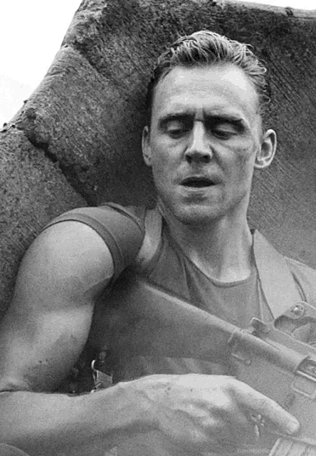 a black and white photo of a man with his eyes closed holding a gun