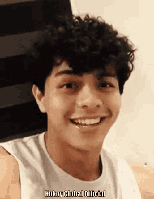 a young man with curly hair is smiling and the words kokoy global official are on the bottom
