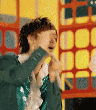 a man in a green jacket is singing into a microphone while covering his face with his hand .