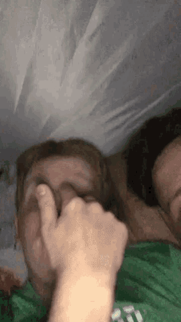 a man in a green shirt is covering his face with his hand while another man sleeps next to him .
