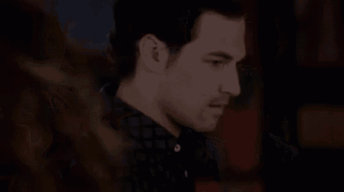 a man in a black shirt is sitting at a table in a dark room .