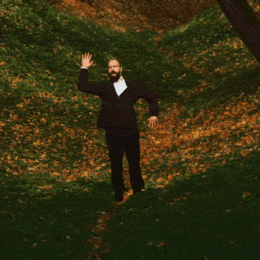 a man with a beard and glasses is standing in a field waving