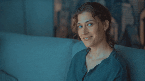 a woman is smiling while sitting on a couch in a blue shirt