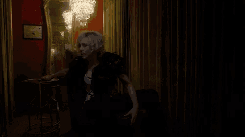 a woman sitting in a dark room with a chandelier in the background