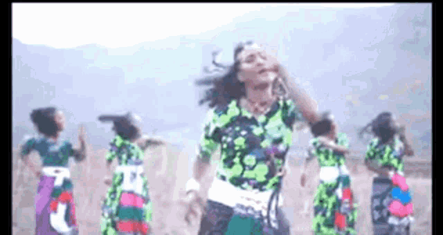 a group of women in colorful dresses are dancing in a field with mountains in the background .