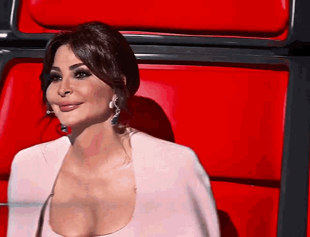 a woman with a very large breast is sitting in a red chair and smiling