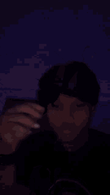a young man is taking a selfie with his phone in the dark while wearing a ring on his finger .