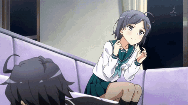 a girl in a school uniform is sitting on a couch next to a boy with a tbs logo on the wall