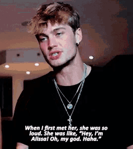 a man wearing a black shirt and a necklace is talking to someone .