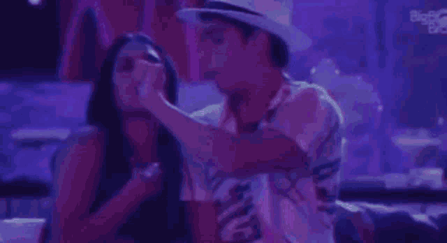 a man and a woman are dancing in a club . the man is wearing a hat .