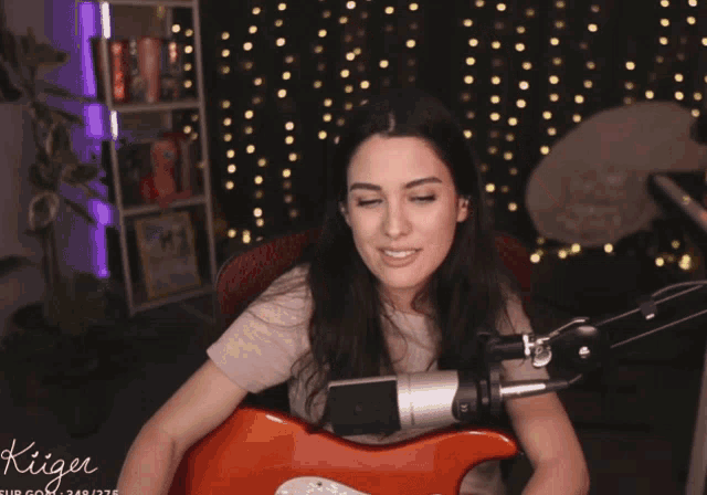 a woman is playing a guitar in front of a microphone with the name kiger on the bottom