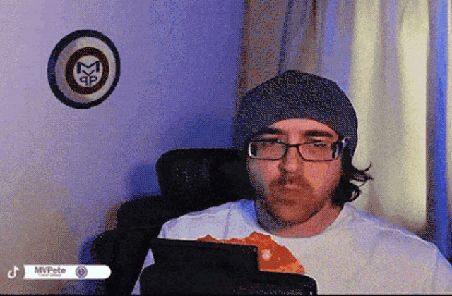 a man wearing a beanie and glasses is sitting in front of a mvpete sign