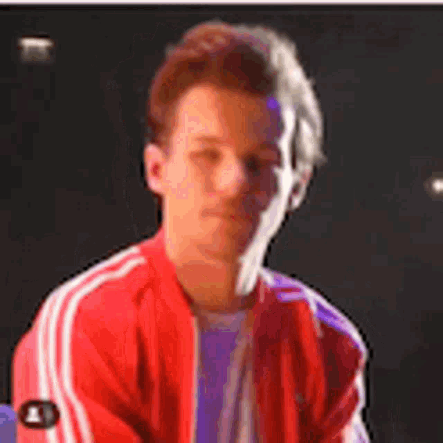 a man in a red jacket with white stripes on the side is sitting in front of a black background .