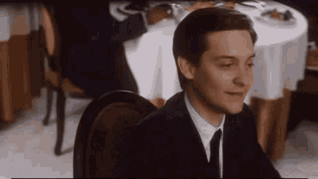 a man in a suit and tie is sitting in a chair in front of a table .
