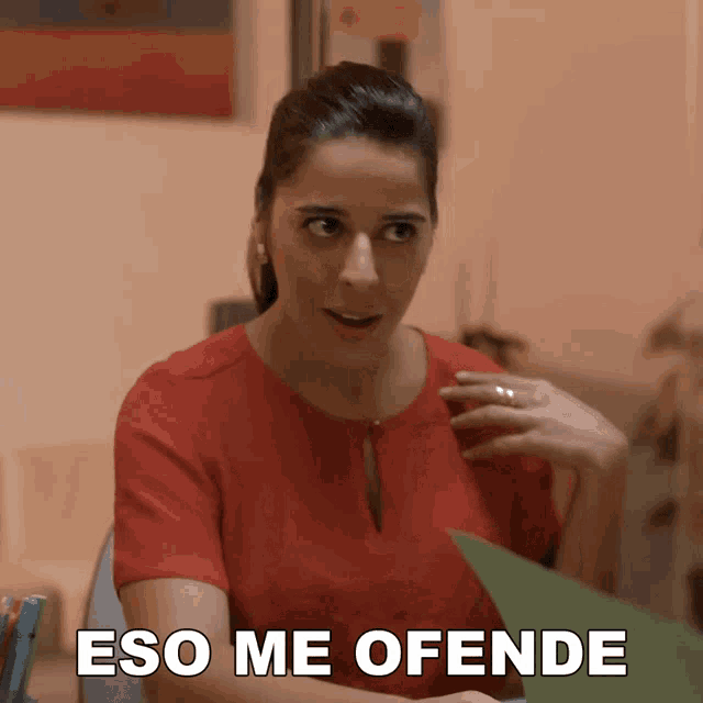 a woman in a red shirt is sitting at a desk with the words eso me ofende behind her